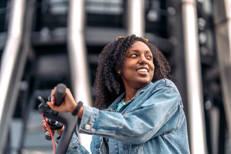 Pretty african woman with curly hair having fun in the city riding her electric scooter.の写真素材
