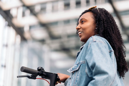 Pretty african woman with curly hair having fun in the city riding her electric scooter.の写真素材