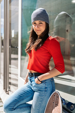 Pretty young woman in casual clothes holding her long-board and looking at camera.の写真素材
