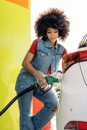 Beautiful woman with afro hair filling her car with gasoline at the gas station.の写真素材