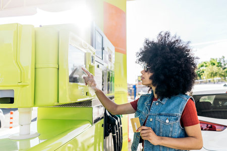 Beautiful woman with afro hair paying with her credit card after filling her car with gasoline at...