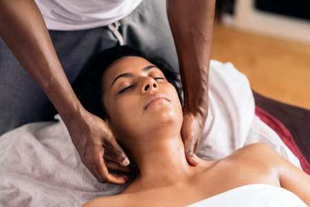 Relaxed woman lying down and receiving a neck massage. The masseuse is a handsome African American...