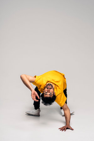 Energetic male dancer wearing casual clothes doing bridge handstand in studio shot and looking at...