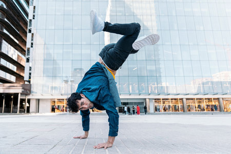 Talented young man with casual clothes doing break moves in the street against big modern buildings...