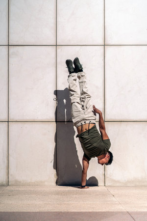 Confident young boy doing break dance moves against white wall in the street.