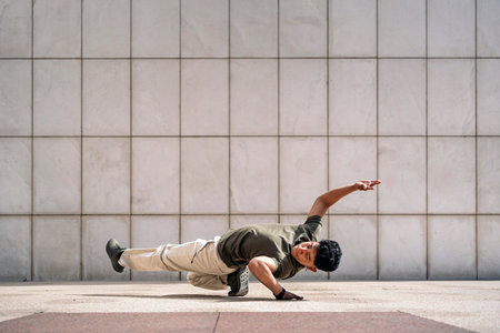 Cool young latin man doing break dance moves in the street and showing his talent.