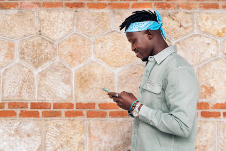 Young and stylish african man using his cellphone against brown wall.の写真素材