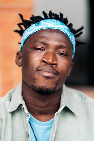 Young african american boy with dreadlocks and blue bandana looking at camera in the city.
