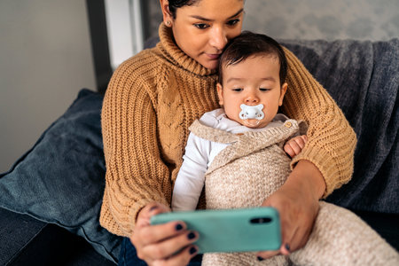 Stock photo of happy mother and her baby watching cartoons on the phone at home.