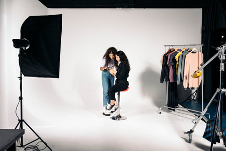 Stock photo of young latin woman doing make up to her client in studio over white background. They are looking for references on the phone.の写真素材