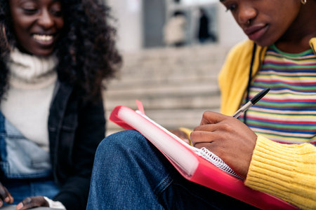 Stock photo of black friends using laptop while sitting on stairs and doing homework.