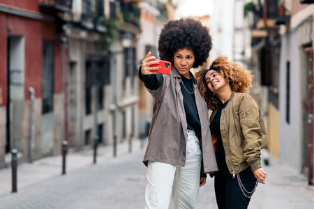 Stock photo of beautiful african american friends taking picture with phone in the street.