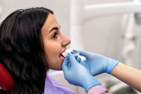 Stock photo of woman sitting in dentist's chair putting on teeth covers.