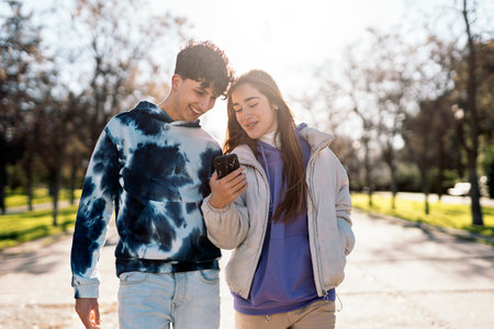 Stock photo of happy friends talking and using phone while walking in the park.