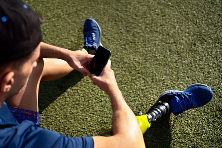 Disabled man athlete using his phone while sitting in the grass.の写真素材