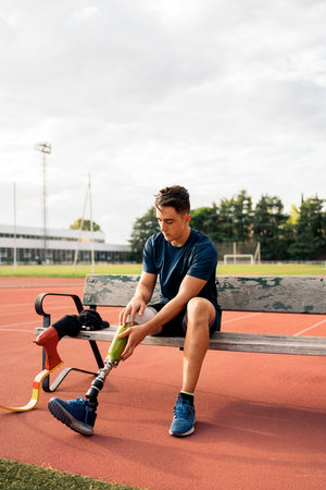 Stock photo of disabled man athlete sitting on a bench and putting on his leg prosthesis.の写真素材