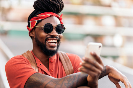 Stock photo of attractive african american boy with dreadlocks and a bandana using his phone. He is laughing.の写真素材