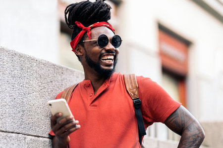 Stock photo of attractive african american boy with dreadlocks and a bandana using his phone. He is laughing.の写真素材