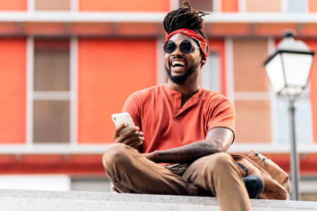 Stock photo of attractive african american boy with dreadlocks and a bandana using his phone. He is laughing.の写真素材