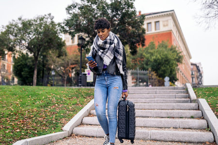 Stock photo of young afro woman with suitcase using her phone.の写真素材