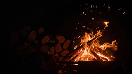 Experience the captivating allure of a burning campfire against the inky night sky. This evocative image features vibrant flames with glowing sparks dancing above a meticulously stacked pile of wood. The burning bonfire creates a cozy, warm ambiance, radiating heat and light. Perfect for illustrating concepts of camping, outdoor adventures, or creating a peaceful background for travel and vacation themes. This detail photograph is ideal for conveying energy and the raw beauty of nature, from embers to logs.の素材