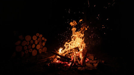 Experience the captivating beauty of a burning campfire under a starlit night sky. This image showcases vibrant flames dancing against the dark backdrop, with mesmerizing sparks illuminating the scene. The wood crackles with heat, creating a warm, cozy glow. Perfect for illustrating camping adventures, outdoor activities, bonfires, or evoking feelings of peaceful solitude. Ideal for websites, blogs, and marketing materials related to travel, nature, and relaxation.の素材