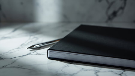 A minimalist black notebook and pen rest elegantly on a polished marble surface, bathed in soft natural light. This sophisticated scene features a clean, modern aesthetic ideal for creative projects, corporate branding, or professional presentations. The blank, hardcover notebook provides space for writing, planning, or journaling. The refined composition evokes a sense of calm, making it perfect for conveying elegance and inspiration in various design applications and workspace themes. This image offers a stylish backdrop for your next project.の素材