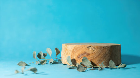 Showcase your products with this stunning wooden log display stand, perfectly set against a vibrant blue backdrop. This image features a natural, rustic wood slice podium adorned with fresh eucalyptus leaves, creating an organic and eco-friendly presentation. Ideal for cosmetics, spa products, or any item needing a modern, minimalist showcase. Use this template to elevate your product presentation with its blank copy space and inviting texture.の素材