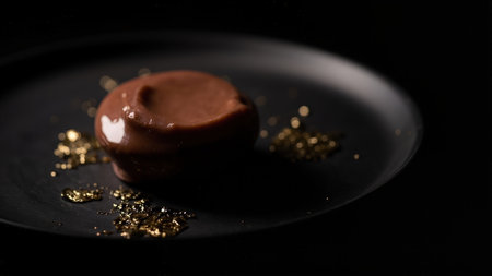 Close-up shot of a decadent chocolate dessert adorned with edible gold flakes, elegantly presented on a black plate.  The rich, smooth texture and luxurious presentation are perfect for showcasing high-end desserts, gourmet food, or fine dining concepts. Ideal for menus, blogs, or culinary publications.の素材