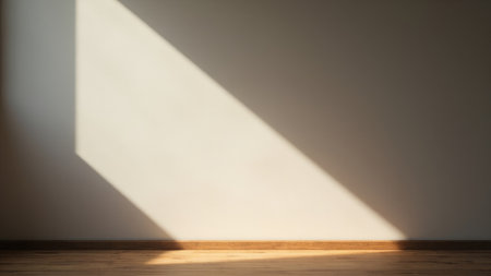 Beige wall with diagonal shadow and wooden floor creating a minimalist interior with natural light.の素材