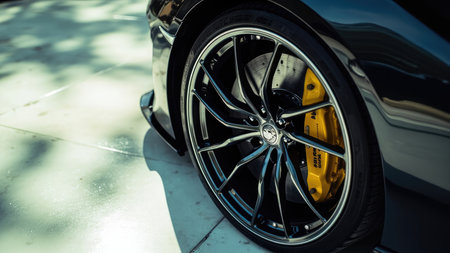 Close-up of a car wheel with a silver rim and yellow brake calipers, set against a light surface with shadows.の素材