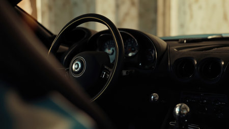 Close-up of a car interior showing a black dashboard with steering wheel, gauges, and gear shift in a dimly lit setting.の素材