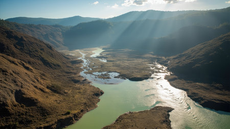 Aerial shot of a river winding through a valley with brown hills and green water under a bright sky.の素材