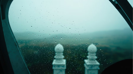 Raindrops on a window obscuring a view of white minarets and a misty green landscape.の素材