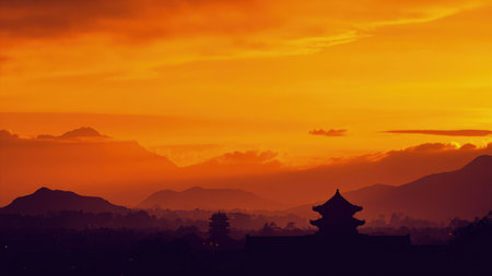 Silhouette of Asian buildings against an orange sunset sky with mountains and clouds.の素材
