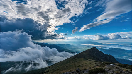 A dramatic cloudscape over a mountain range with blue sky and green slopes. Sunlight pierces through clouds.の素材