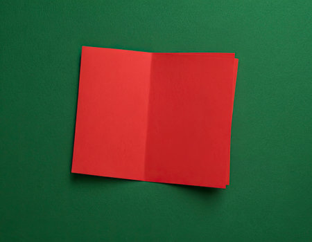 Red paper sheet on green background. Flat lay, top view.の素材