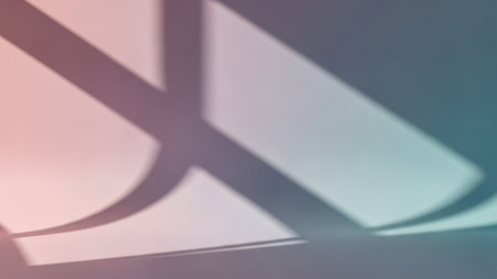 An abstract composition featuring geometric shadow shapes and lines cast across a surface. The background exhibits a soft color gradient transitioning from pinkish hues on the left to teal and blue tones on the right. The shadows create a layered effect with distinct edges and curves, forming an intriguing visual pattern.の素材