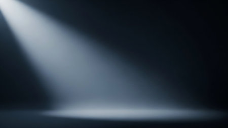 A dramatic beam of white light shines down from the upper left corner onto a dark, reflective floor, creating a spotlight effect. The light creates a bright pool on the floor and fades into the dark background.の素材