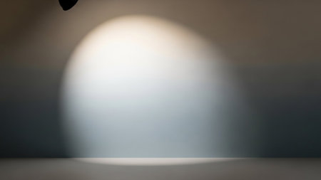 A soft, diffused spotlight beam creates a bright, oval shape on a neutral-toned studio floor. The edges of the light are soft, and a subtle shadow is cast. The background is dark and out of focus, emphasizing the illuminated area. The overall impression is clean, simple, and atmospheric, suitable for product placement or abstract concepts.の素材