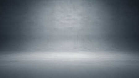 A dark and moody studio background with a subtle textured effect. The floor appears to have a fine grid pattern, and the backdrop fades into a darker gray. Soft lighting creates a gradient effect, casting subtle shadows and highlighting the atmospheric quality of the space.の素材