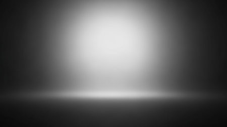 A dark, gradient studio background with a bright, diffused spotlight emanating from the top center. The light creates a luminous circle on the floor and a subtle glow, casting soft shadows. This abstract image is suitable for product displays or presentations.の素材