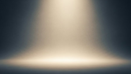 A soft, warm spotlight emanates from the top of the frame, casting a gentle glow downwards onto a textured, dark background. The light creates a subtle gradient, brighter at the bottom where it appears to illuminate a surface, and fading into darkness towards the top. The texture adds a subtle graininess to the overall effect.の素材