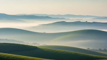 A breathtaking landscape of rolling green hills shrouded in thick fog at sunrise. The soft morning light illuminates the undulating terrain, creating distinct layers of mist that recede into the distance. The scene evokes a sense of peace and tranquility, highlighting the natural beauty of the countryside.の素材