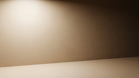 A softly lit corner of an empty room with a textured wall and floor. A warm light source illuminates the upper left portion of the wall, creating a gradient that transitions to shadow on the right. The floor is a lighter, neutral tone. This image evokes a sense of calm and simplicity, suitable for various presentation or background needs.の素材