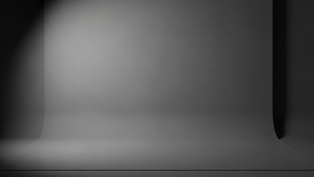 An empty photography studio with a seamless gray backdrop curving from the wall to the floor. A soft spotlight illuminates the upper left portion of the background, creating subtle shadows and a gradient effect. The space is minimalist and neutral, suitable for various shooting purposes.の素材