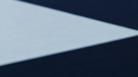 A minimalist abstract image featuring a sharp diagonal line of light cutting across a dark, textured surface. The light creates a bright, soft-edged area that contrasts with the deep, rich darkness of the surrounding area. The texture of the surface is subtly visible, adding depth to the composition.の素材