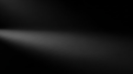 A dark, abstract background with a subtle texture. A soft spotlight emanates from the left side, casting a gradient of light and shadow across the surface. The lighting is diffused, creating a moody and atmospheric feel with ample copy space.の素材