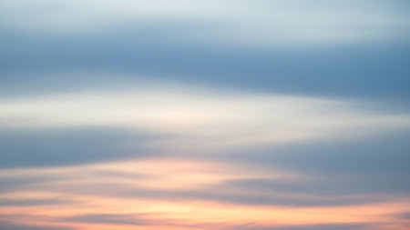 A soft-focus image of a sunset sky with diffused clouds in pastel hues of blue, white, and peach. The gentle blending of colors creates an atmospheric and serene background, evoking a sense of tranquility and peace.の素材