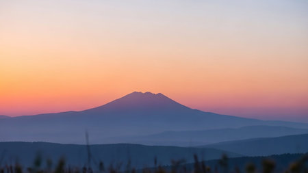 A serene mountain range silhouetted against a vibrant sunset sky with soft gradients of orange, pink, and purple.の素材